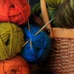 Red, Blue, and Green yarn balls with knitting needles near a wicker basket.