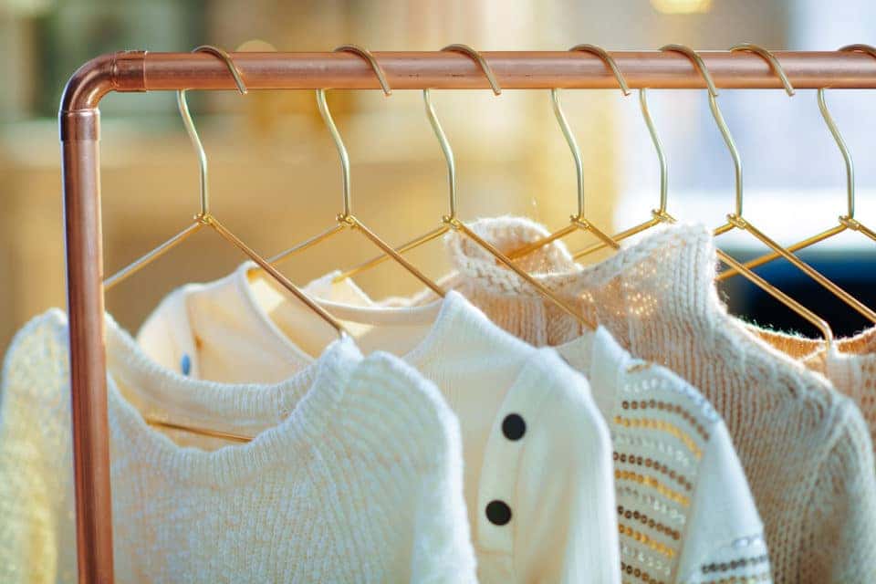 Closeup on modern copper clothes rack with sweaters on hangers.