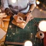 Hipster man with tattoo on his hand sitting at work and wrapping gift box.