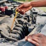 hands pulling oil dipstick under hood of car