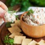 Smoked salmon, cream cheese and dill dip in wooden bowl served with gluten free crackers on round cutting board