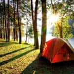 an orange tent in the woods by a pond