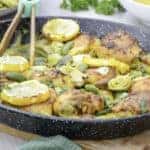 Crispy baked chicken thighs and drumsticks stew with artichokes hearts, green olives, roasted lemon slices, seasoning and onions served in a black enamelled pan on a wooden cutting board