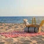 Blanket with picnic basket on sandy beach near sea