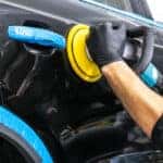 Car polish wax worker hands applying protective tape before polishing. Buffing and polishing car. Car detailing. Man holds a polisher in the hand and polishes the car