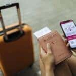 Young female is sitting at the airport holding a passport and a phone while waiting for a flight