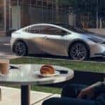 Couple in coffee shop looking out the window at 2024 silver Prius