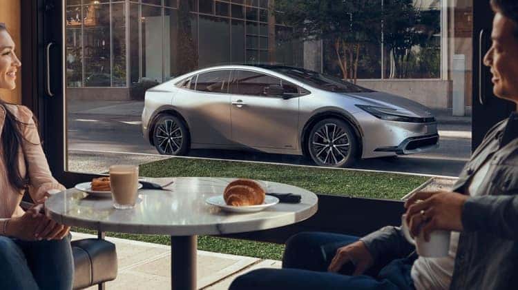 Couple in coffee shop looking out the window at 2024 silver Prius
