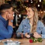 Coffee shop, date and couple of friends with rose for valentines day, anniversary or love in restaurant bokeh. Happy diversity people or woman with love partner at cafe at night for social talking