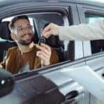 Happy man receiving keys for his new car in a showroom