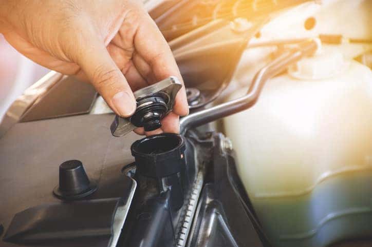 Don't Overlook Your Radiator & Cooling System -- Hand is opening the radiator cap to check the coolant level