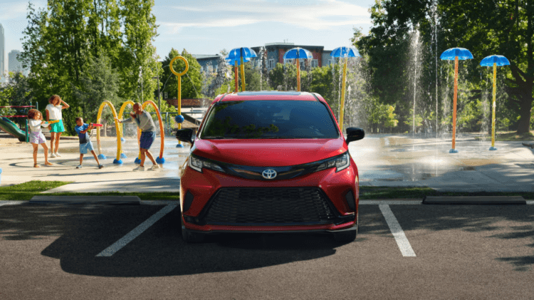 Sienna Family Vacation Choice: Parked red Toyota Sienna outside of a waterpark with a family playing in the water.