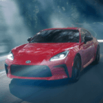 Red Toyota GR86 driving on a road surrounded by the woods
