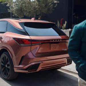 A Lexus RX 500h F Sport parked on a city street with a man walking past, showcasing its sporty stance and bold design.