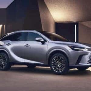 A silver Lexus RX 500h plugged into a home EV charger, parked outside a modern house at dusk.