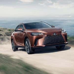 Lexus RX in copper color driving on a coastal dirt road with scenic ocean views in the background.