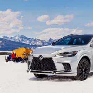 Lexus RX parked on a snowy plain with a group of people camping in the background, featuring a mountain range.