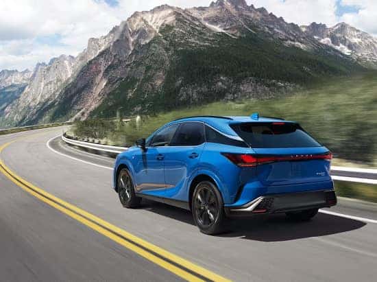 A blue Lexus RX driving along a scenic mountain highway with a stunning backdrop.