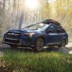 blue subaru outback off roading in a forested area