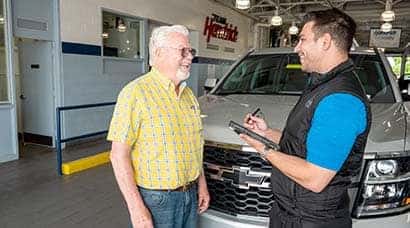 A woman sitting at a table inside a car dealership talking to another woman.