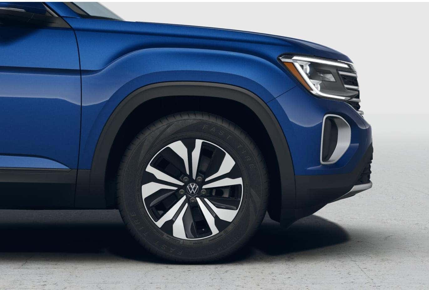 Close-up of the blue 2026 Volkswagen Atlas front wheel, fender, and LED headlight.