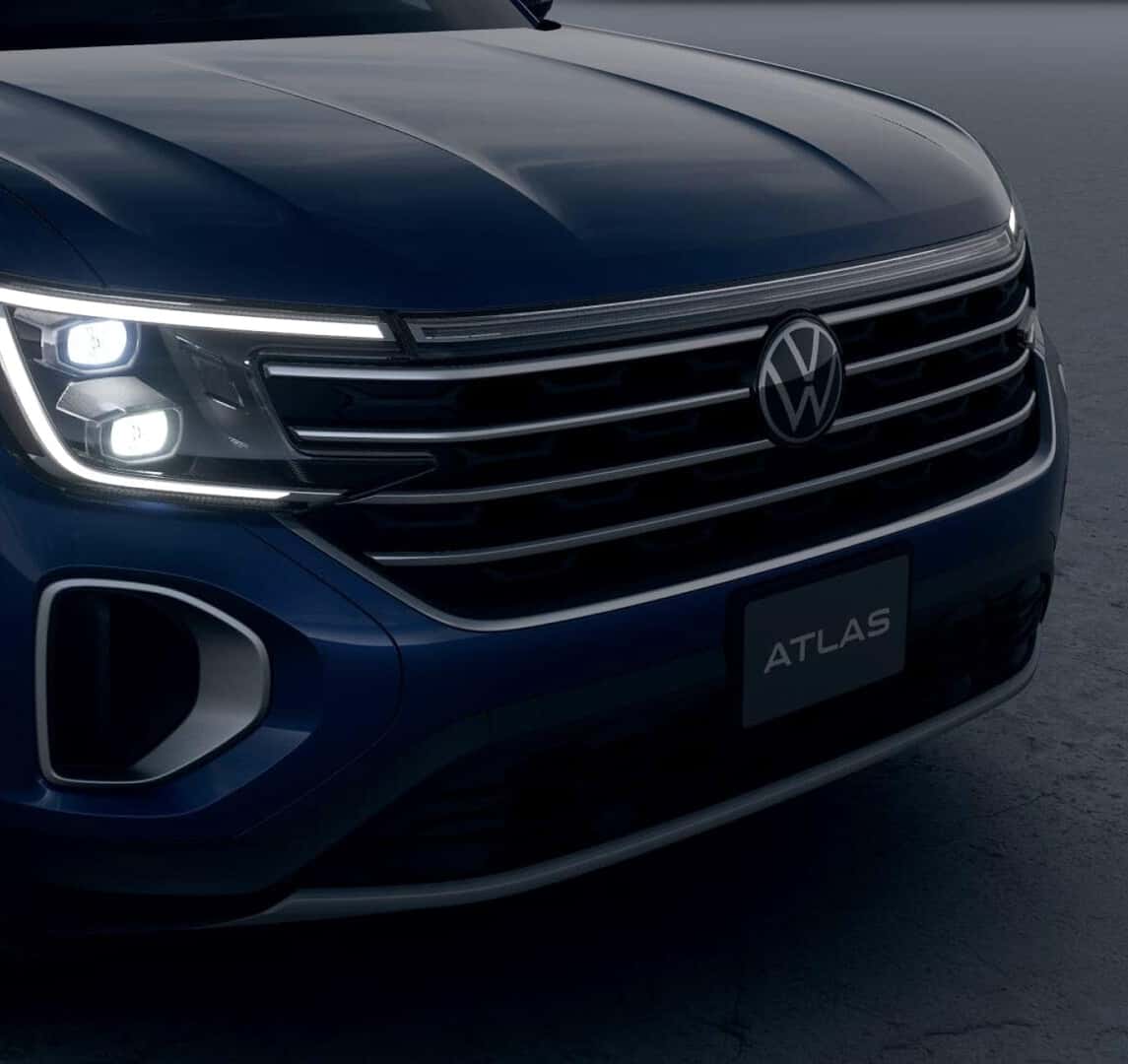 Close-up of the blue 2026 Volkswagen Atlas front grille and illuminated LED headlights.