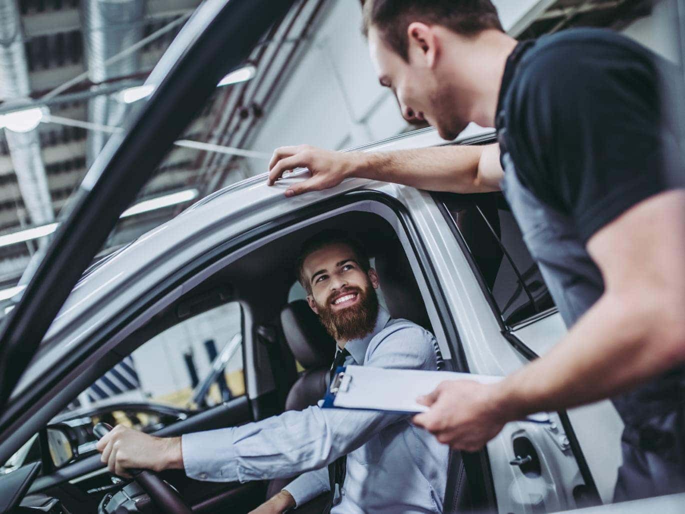 Automotive technician speaking with a driver seated inside a vehicle during a service inspection.
