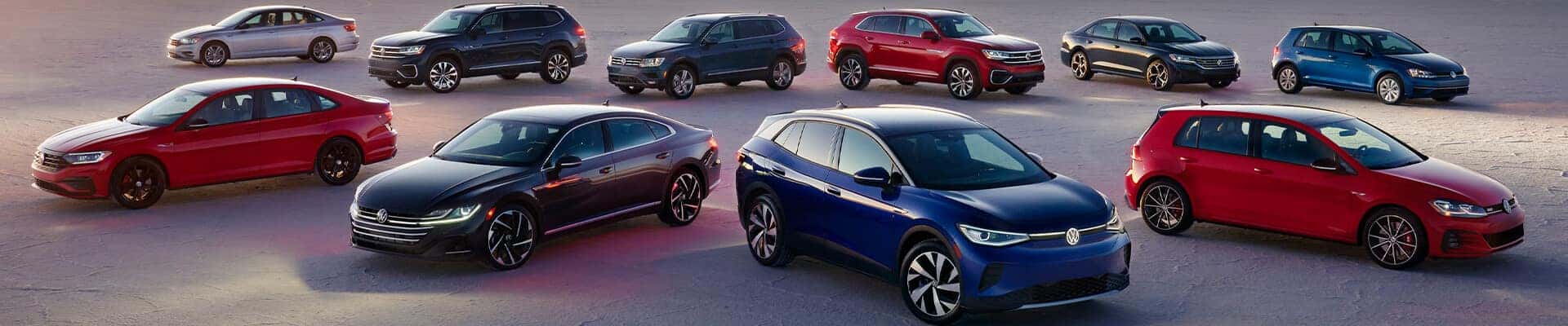 The 2023 Volkswagen lineup of Cars and SUVs parked in a clear gray lot at dusk.