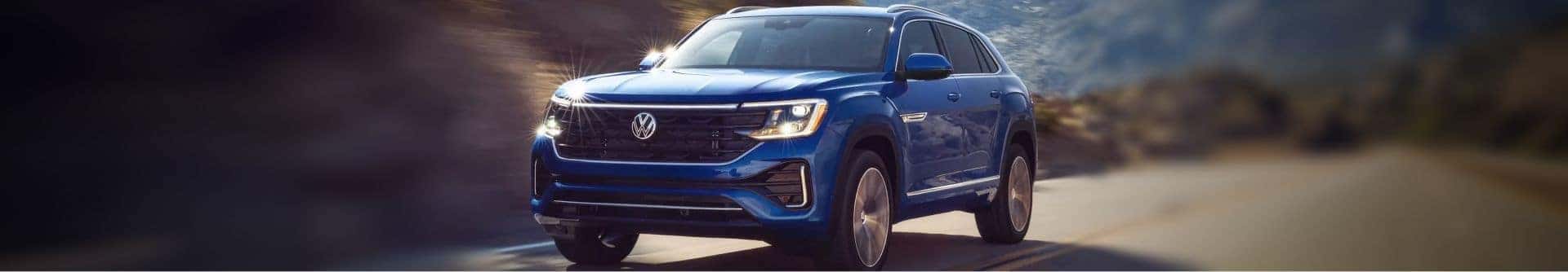 Blue Volkswagen SUV driving on a scenic road with its headlights illuminated.