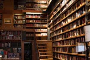 Large library with staircase leading upstairs with hundreds of books lining the walls.