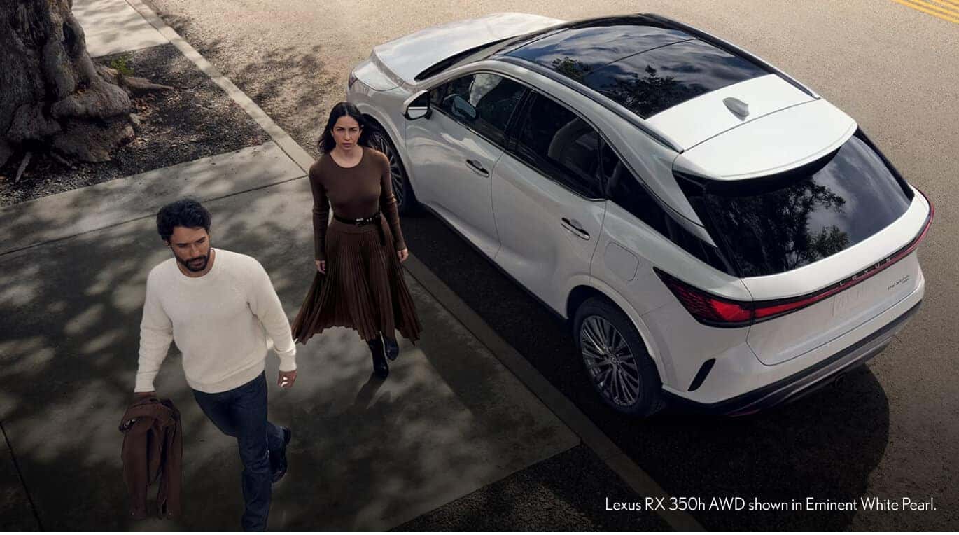 High-angle view of Lexus RX 350h AWD in Eminent White Pearl with two people walking alongside.