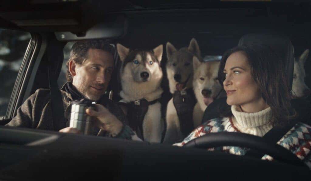 Woman and Man Sitting in the Front Seats of a Lexus GX with Huskies in the Back Seats in Sled Dogs Advertisement