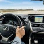 Customer test-driving a Lexus SUV on a scenic road near Lexus of Mobile, with interior view showing driver interacting with vehicle features.