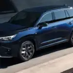 Blue 2025 Lexus TX 350 SUV driving on a modern city road, showcasing its sleek exterior design and premium styling – available at Lexus of Mobile.