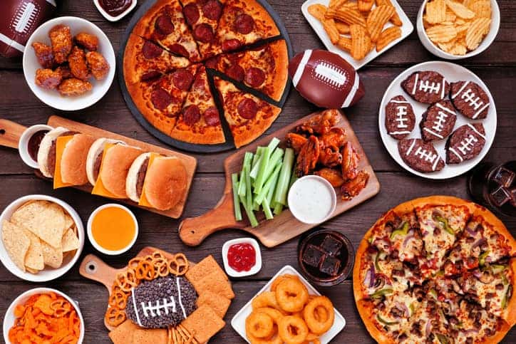 Score a Touchdown With These Super Bowl Appetizers - picture of a table spread with classic football game food like pizza, chips, wings, and hamburgers.