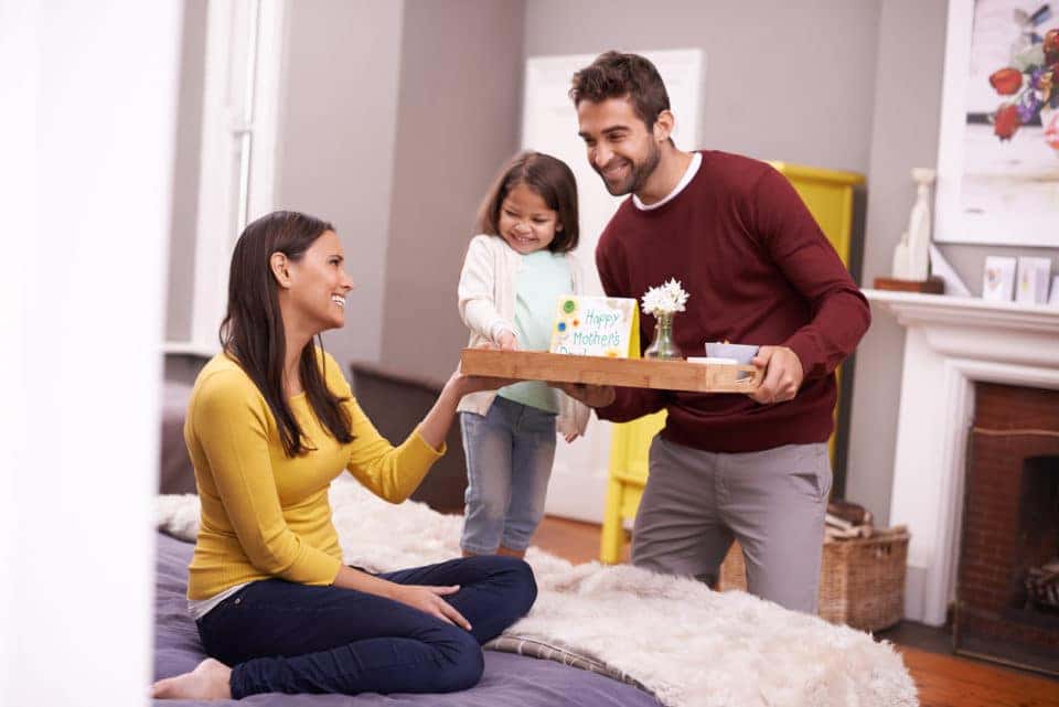 A man and his daughter bringing his wife breakfast in bed on Mother's day