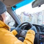 woman driving a car in cold weather wearing a yellow coat and a gray hat and gloves.