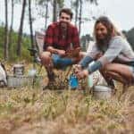 Man and woman camping in a small clearing. Backdrop of trees.