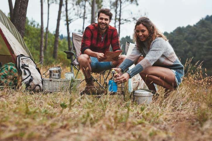 Man and woman camping in a small clearing. Backdrop of trees.