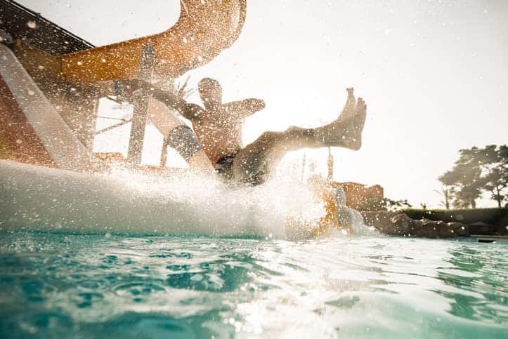Playful man having fun while sliding into the water with his arms outstretched at amusement park.