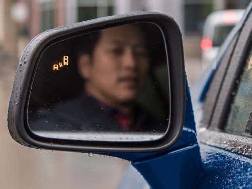 2024 Chevy Tahoe close up view of man looking in side mirror with blind spot monitor light on