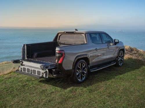 2025 GMC Sierra EV Denali rear exterior view of truck parked on a hill with tailgate down