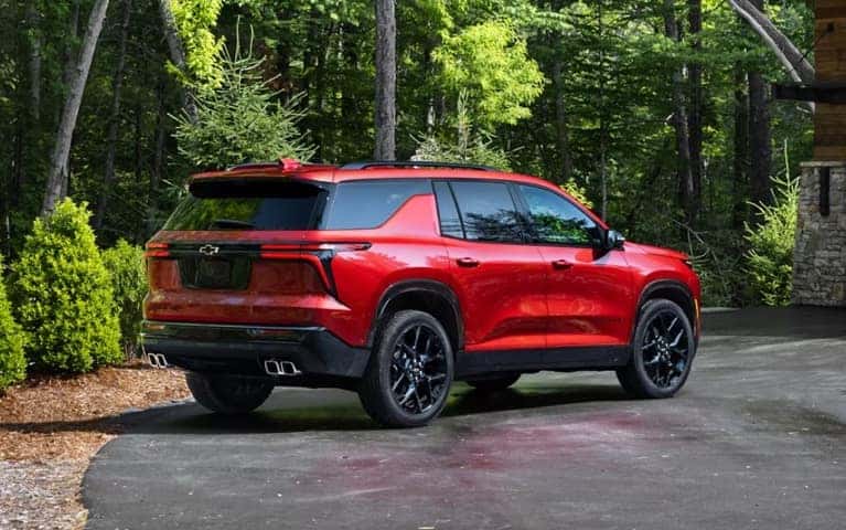 Chevrolet SUV parked by a green forest of tall evergreens.