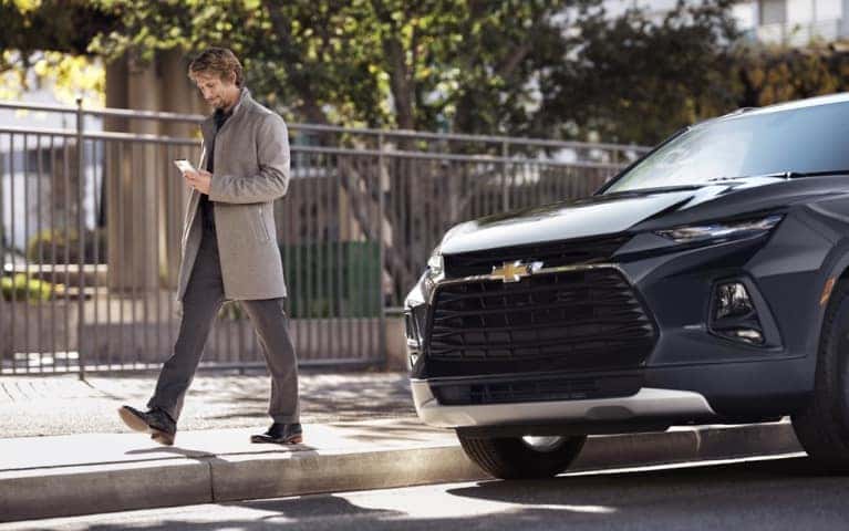 Well dressed man on his mobile phone walking on the sidewalk from a parked Chevrolet SUV.