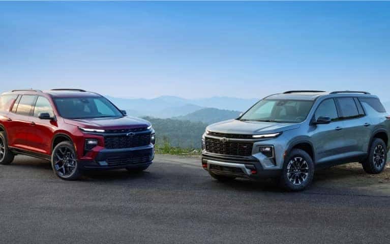 Two Chevy SUV's parked at the edge of a bluff overlooking a forested valley.