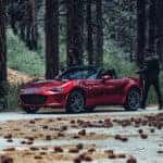 A red 2020 Mazda Miata in a forest; a couple is about to enter the vehicle.