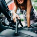 Happy woman cleans the interior of her car with vacuum cleaner.