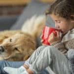 Two children and a dog sitting together on a couch drinking hot chocolate