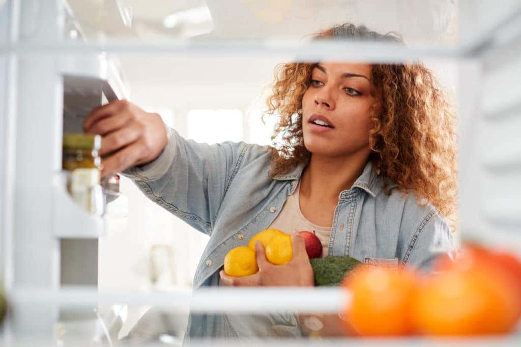 Woman Opens Fridge Door And Packs Food Onto Shelves