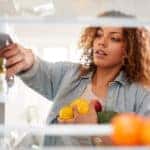 Woman Opens Fridge Door And Packs Food Onto Shelves